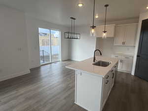 Kitchen with pendant lighting, sink, white cabinets, a kitchen island with sink, and light stone countertops