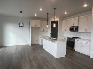 Kitchen featuring white cabinetry, decorative light fixtures, an island with sink, and appliances with stainless steel finishes