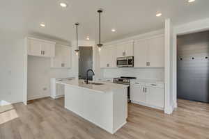 Kitchen with a sink, light wood-type flooring, a center island with sink, and stainless steel appliances