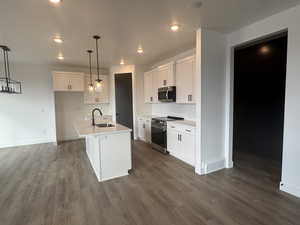 Kitchen with an island with sink, appliances with stainless steel finishes, pendant lighting, and white cabinets