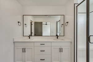 Full bathroom featuring a sink, double vanity, a stall shower, and a ceiling fan