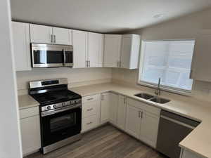 Kitchen featuring appliances with stainless steel finishes, white cabinetry, lofted ceiling, and sink