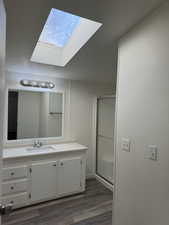 Bathroom featuring a shower with door, a skylight, vanity, and hardwood / wood-style flooring