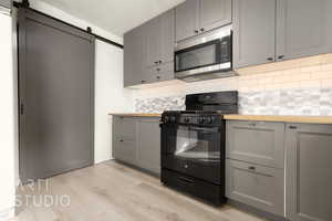 Kitchen featuring a barn door, gray cabinets, gas stove, butcher block countertops, and tasteful backsplash