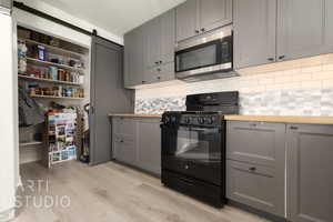 Kitchen featuring butcher block countertops, black gas stove, gray cabinetry, and decorative backsplash