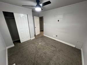 Unfurnished bedroom featuring dark carpet, a closet, ceiling fan, and ornamental molding