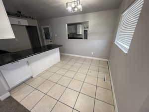 Kitchen featuring white cabinets, an inviting chandelier, light tile patterned flooring, and hanging light fixtures