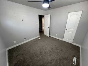 Unfurnished bedroom featuring dark colored carpet and ceiling fan