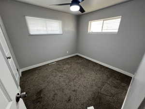 Spare room with ceiling fan and dark colored carpet