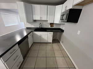 Kitchen featuring stainless steel appliances, white cabinetry, light tile patterned floors, and sink