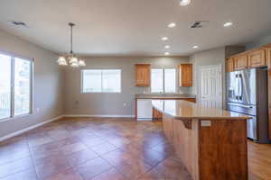 Kitchen and dining areas featuring tile floors, white dishwasher, stainless steel fridge with ice dispenser, hanging light fixtures, a kitchen island, and a notable chandelier