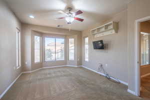 Carpeted primary bedroom featuring bay windows and a ceiling fan