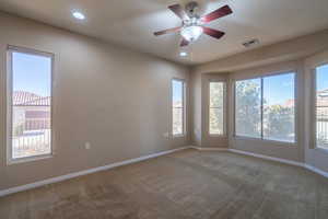 Carpeted primary bedroom featuring bay windows and a ceiling fan