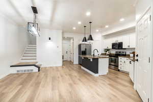 Kitchen featuring decorative light fixtures, appliances with stainless steel finishes, a kitchen island with sink, and white cabinetry