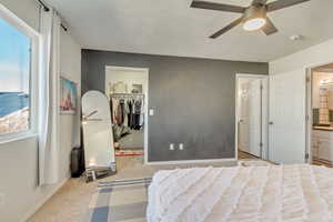 Carpeted bedroom featuring ensuite bathroom, a closet, ceiling fan, and a spacious closet