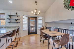 Dining area with light wood-type flooring, vaulted ceiling, and a notable chandelier