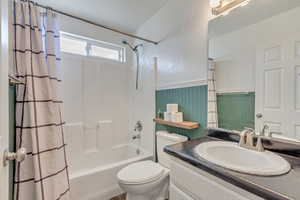 Full bathroom with toilet, shower / bath combo with shower curtain, wooden walls, and vanity