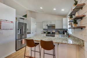 Kitchen featuring stainless steel appliances, sink, light stone counters, lofted ceiling, and kitchen peninsula