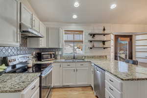 Kitchen featuring kitchen peninsula, light hardwood / wood-style flooring, stainless steel appliances, white cabinetry, and sink