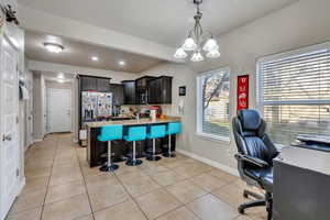 Kitchen featuring light tile patterned floors, dark brown cabinets, a breakfast bar, a notable chandelier, and appliances with stainless steel finishes