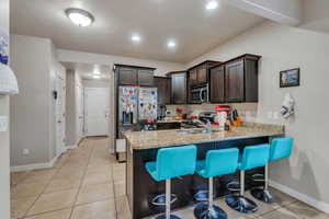 Kitchen with kitchen peninsula, sink, a breakfast bar area, appliances with stainless steel finishes, and dark brown cabinetry