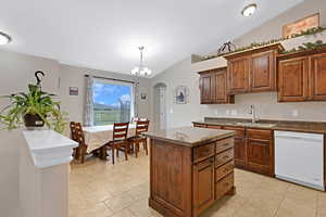 Kitchen with sink, vaulted ceiling, dishwasher, hanging light fixtures, and a kitchen island