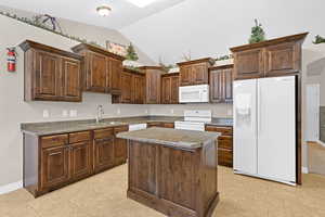 Kitchen featuring white appliances, a center island, lofted ceiling, dark brown cabinets, and sink