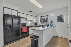 Kitchen with kitchen peninsula, light tile patterned floors, black appliances, backsplash, and white cabinets