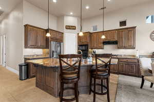 Kitchen with a high ceiling, a kitchen island with sink, black appliances, and pendant lighting