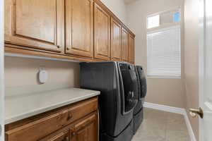 Washroom featuring washer and clothes dryer, light tile patterned floors, and cabinets