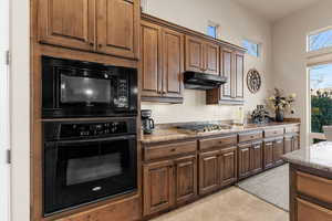 Kitchen featuring black appliances, light tile patterned flooring, and light stone countertops