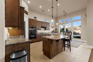 Kitchen featuring sink, pendant lighting, black appliances, light stone countertops, and a kitchen island with sink