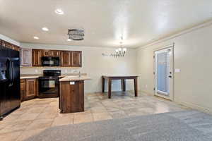 Kitchen with pendant lighting, black appliances, an inviting chandelier, light tile patterned floors, and a center island with sink