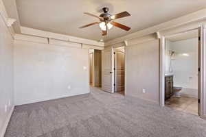 Unfurnished bedroom featuring ensuite bathroom, light colored carpet, and ceiling fan