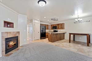 Kitchen featuring decorative light fixtures, black appliances, kitchen peninsula, a tiled fireplace, and light tile patterned floors