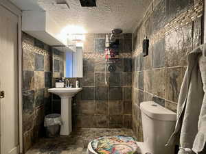 Bathroom with toilet, a textured ceiling, a shower, and tile walls