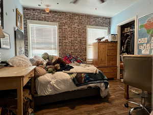 Bedroom with brick wall, wood-type flooring, a closet, and ceiling fan