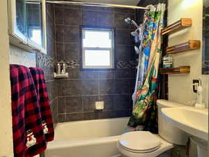 Full bathroom with toilet, shower / bathtub combination with curtain, a wealth of natural light, and sink