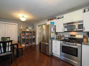 Kitchen with appliances with stainless steel finishes, dark hardwood / wood-style flooring, white cabinetry, and dark stone counters