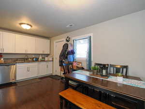 Kitchen with stainless steel dishwasher, a textured ceiling, dark hardwood / wood-style floors, white cabinets, and sink