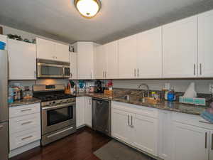 Kitchen with stainless steel appliances, a textured ceiling, white cabinets, and sink