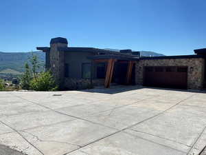 View of front of property featuring driveway, an attached garage, stone siding, a mountain view, and a chimney