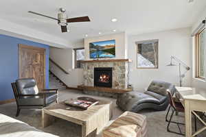 Living room with ceiling fan, carpet floors, and a stone fireplace