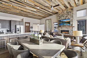 Dining area with a stone fireplace, ceiling fan, sink, high vaulted ceiling, and light hardwood / wood-style flooring