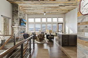 Living room with dark wood-type flooring, a stone fireplace, and ceiling fan