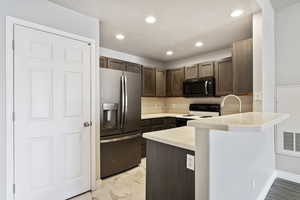 Kitchen with stainless steel refrigerator with ice dispenser, dark brown cabinetry, kitchen peninsula, and range with electric stovetop