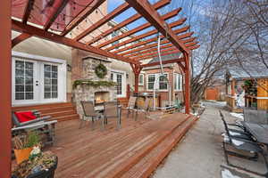 Deck with an outdoor stone fireplace, french doors, and a pergola