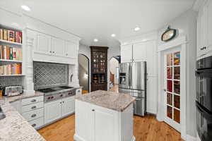 Kitchen featuring light stone countertops, white cabinets, stainless steel appliances, decorative backsplash, and light wood-type flooring