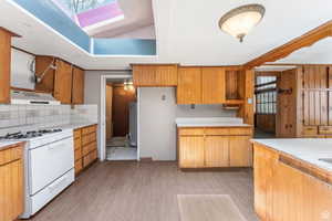 Kitchen with light hardwood / wood-style floors, decorative backsplash, a healthy amount of sunlight, water heater, and white gas range