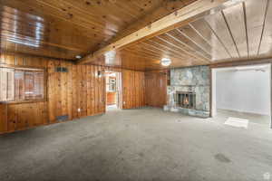 Unfurnished living room featuring carpet, beam ceiling, wood ceiling, and a fireplace